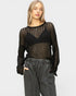 Woman wearing a sheer black and gold sweater with gray pants on a white background