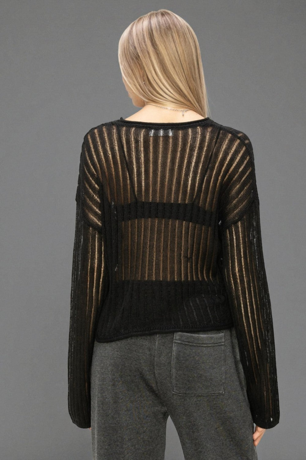 Person wearing a black and gold striped sweater with sheer panels on a gray background
