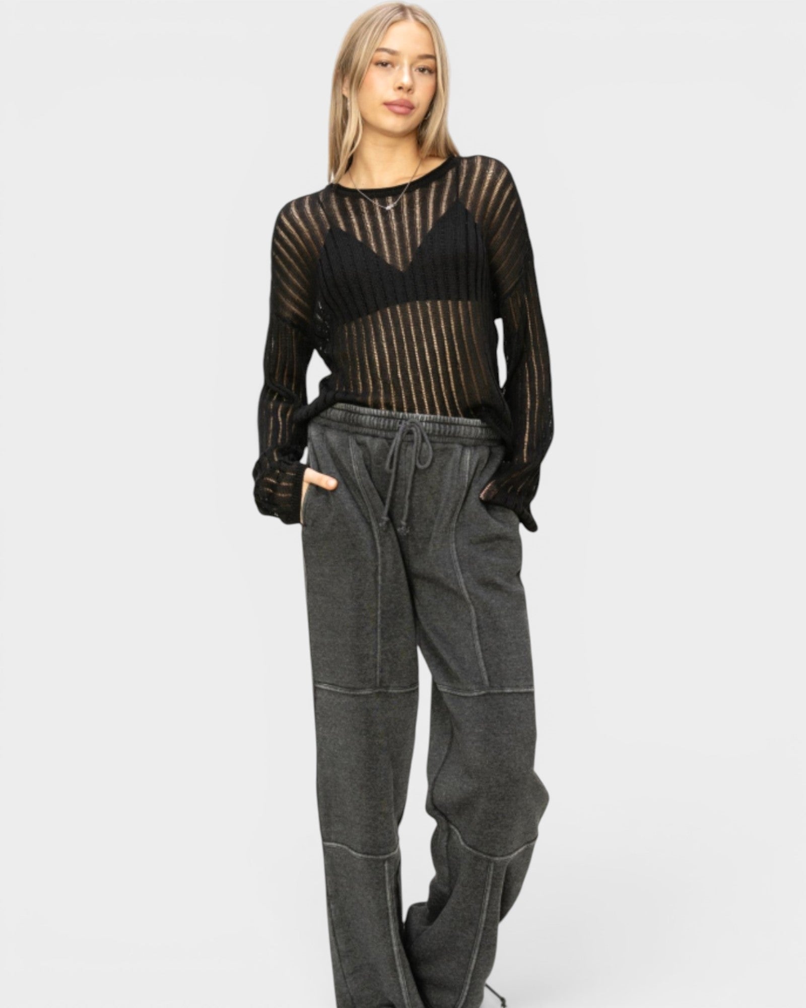 Woman wearing a black sheer top and gray pants on a white background