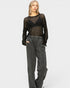 Woman wearing a black sheer top and gray pants on a white background
