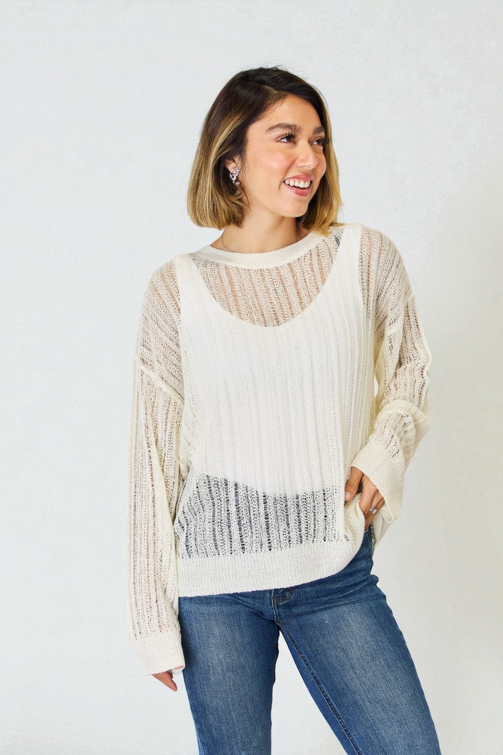 Woman wearing a cream-colored sweater with a textured pattern and blue jeans on a white background
