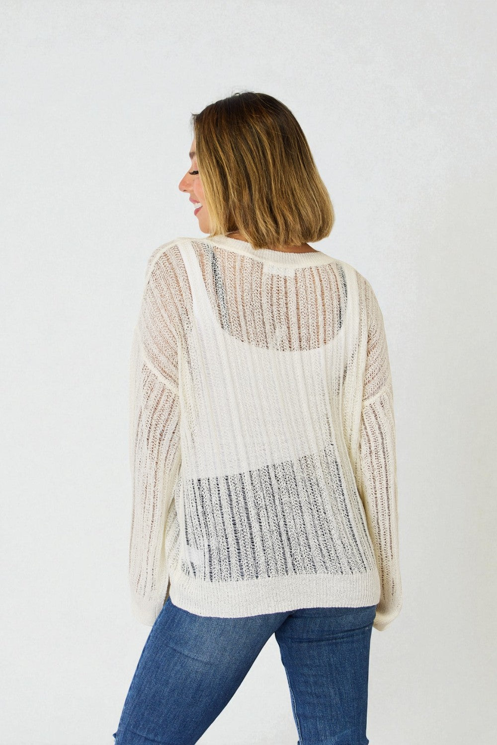 Woman wearing a white knit cardigan with a textured pattern on a plain background