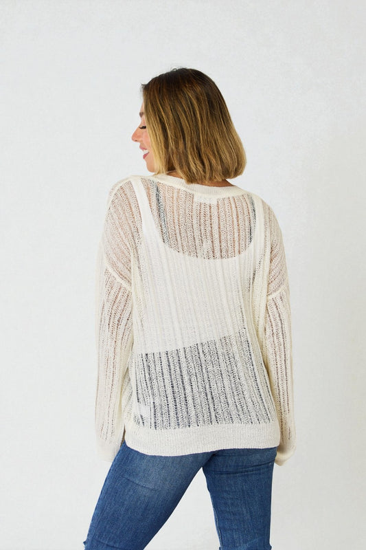 Woman wearing a white knit cardigan with a textured pattern on a plain background