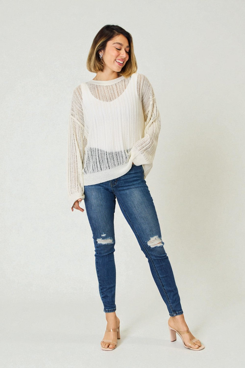 Woman wearing a white knit sweater and blue jeans on a plain background