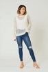 Woman wearing a white knit sweater and blue jeans on a plain background