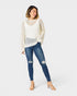 Woman wearing a white knit cardigan, white top, and blue jeans on a white background