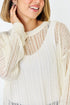 Woman wearing a beige knit cardigan over a white top on a plain background