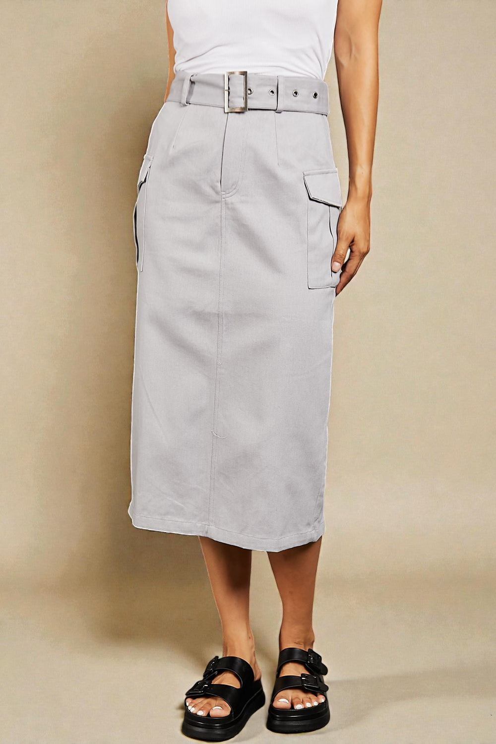 Person wearing a light gray skirt with a belt on a beige background