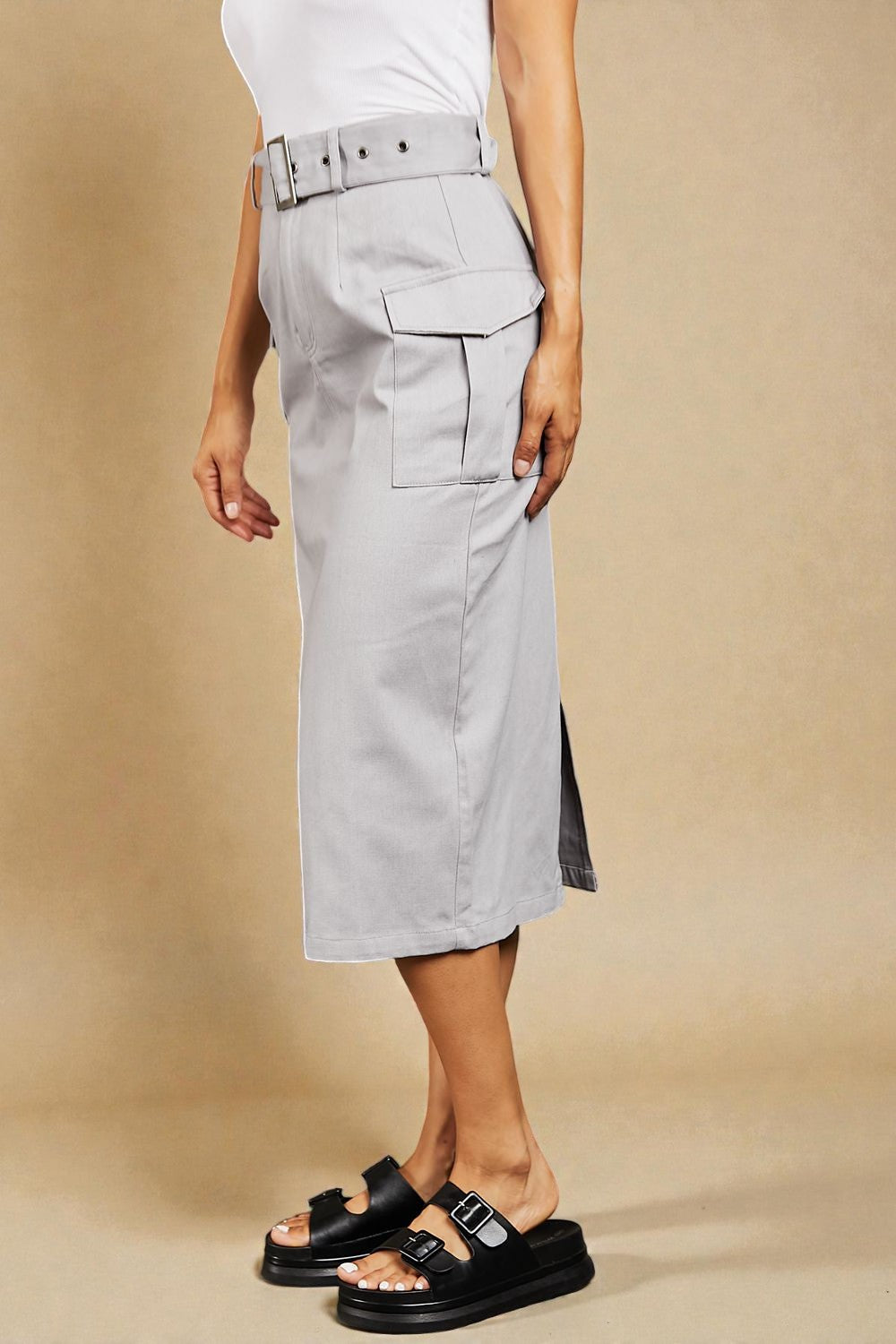 Person wearing a light gray skirt with a belt on a beige background