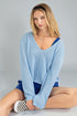 Woman wearing a light blue sweater and blue shorts sitting on a gray background