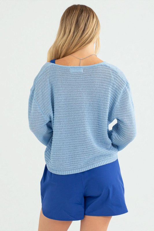 Woman wearing a light blue knitted sweater and blue shorts on a white background