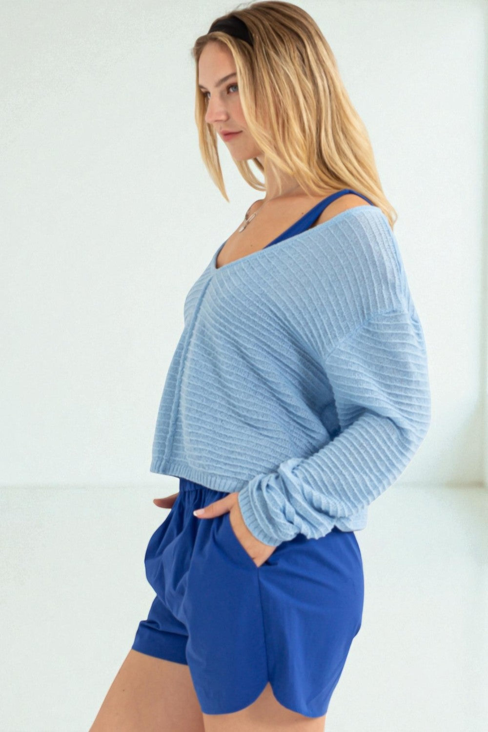 Woman wearing a light blue sweater and blue shorts against a white background