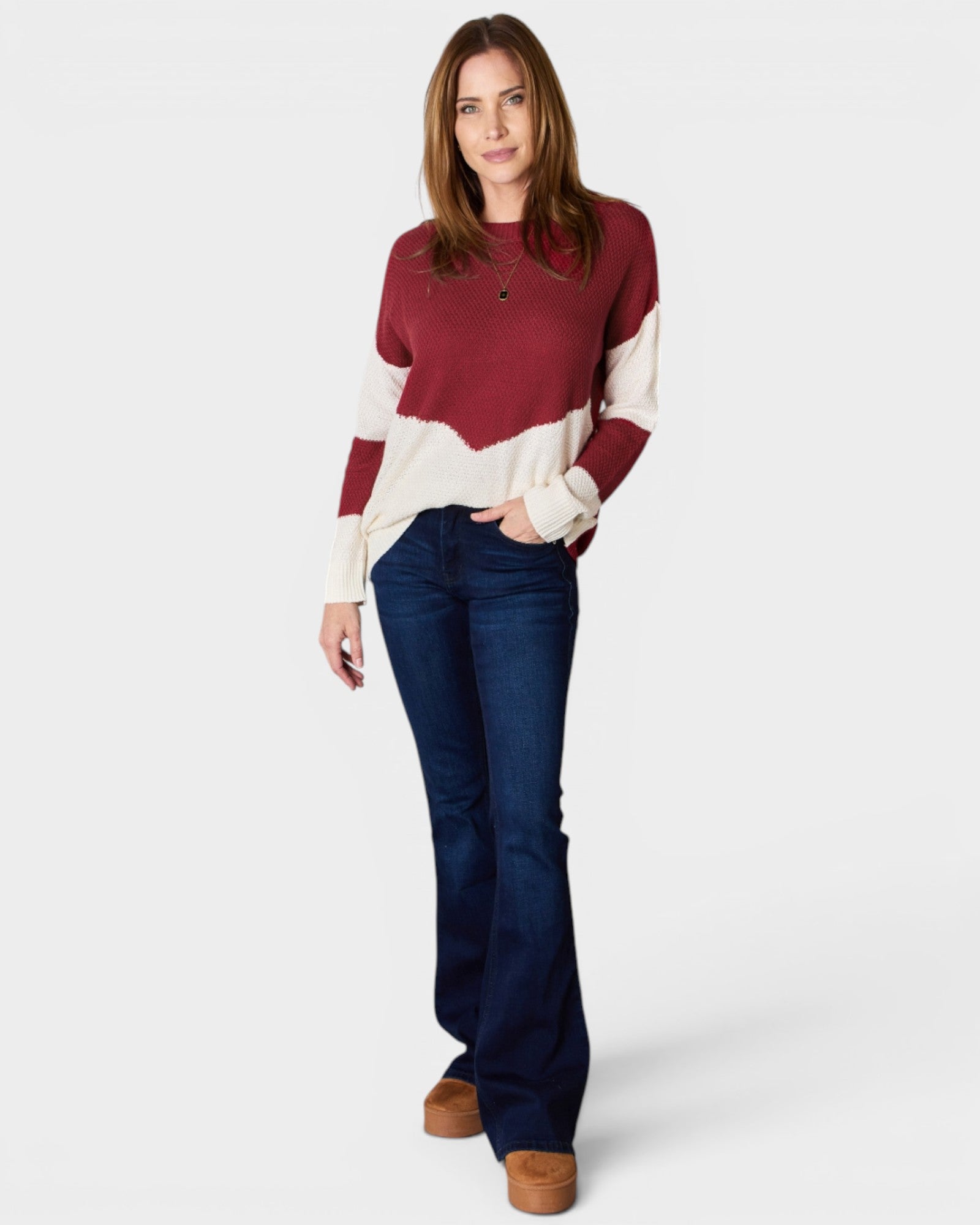Woman wearing a maroon and beige sweater with blue jeans on a white background