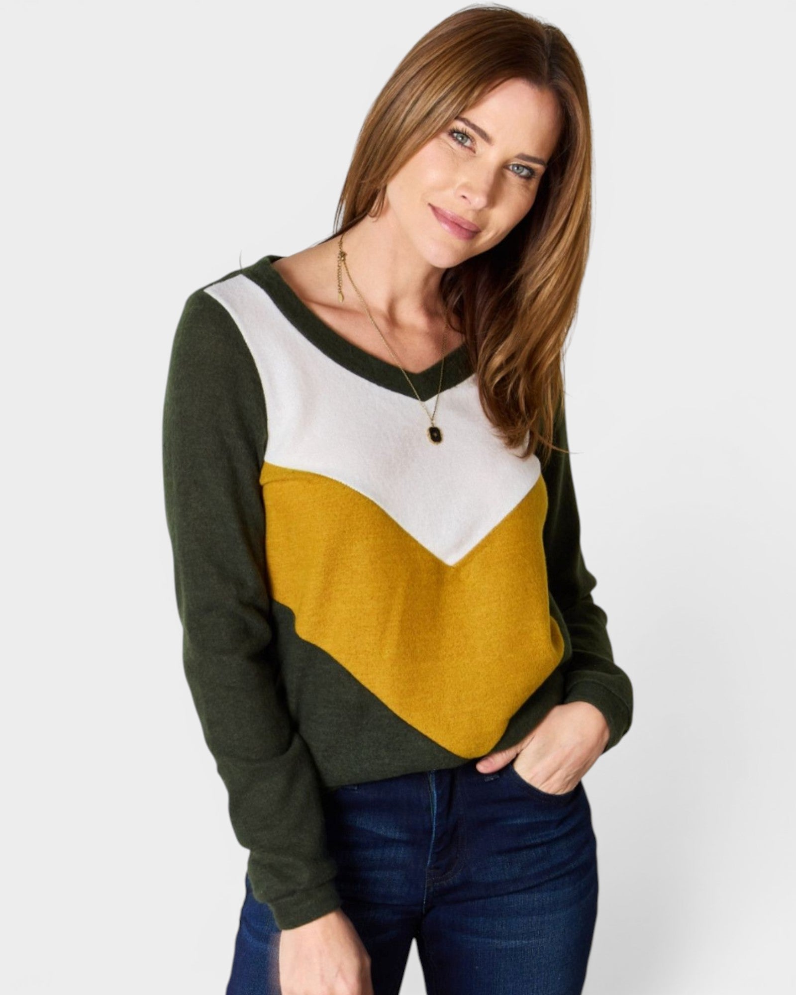 Woman wearing a green, white, and mustard color-blocked sweater on a plain background