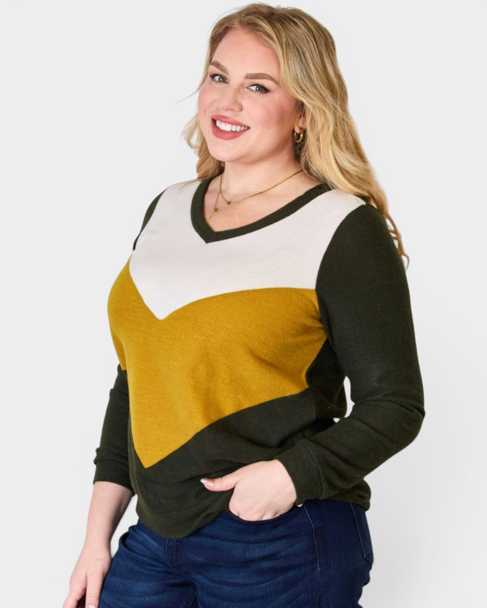 Woman wearing a color-blocked sweater with black, mustard yellow, and white sections on a plain background.