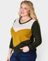 Woman wearing a color-blocked sweater with black, mustard yellow, and white sections on a plain background.