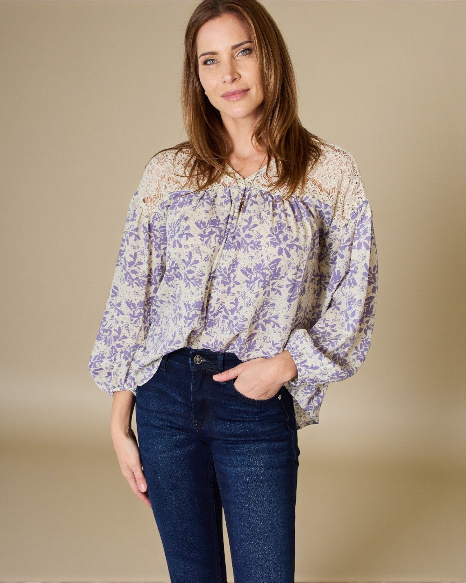 Woman wearing a floral blouse and jeans against a beige background