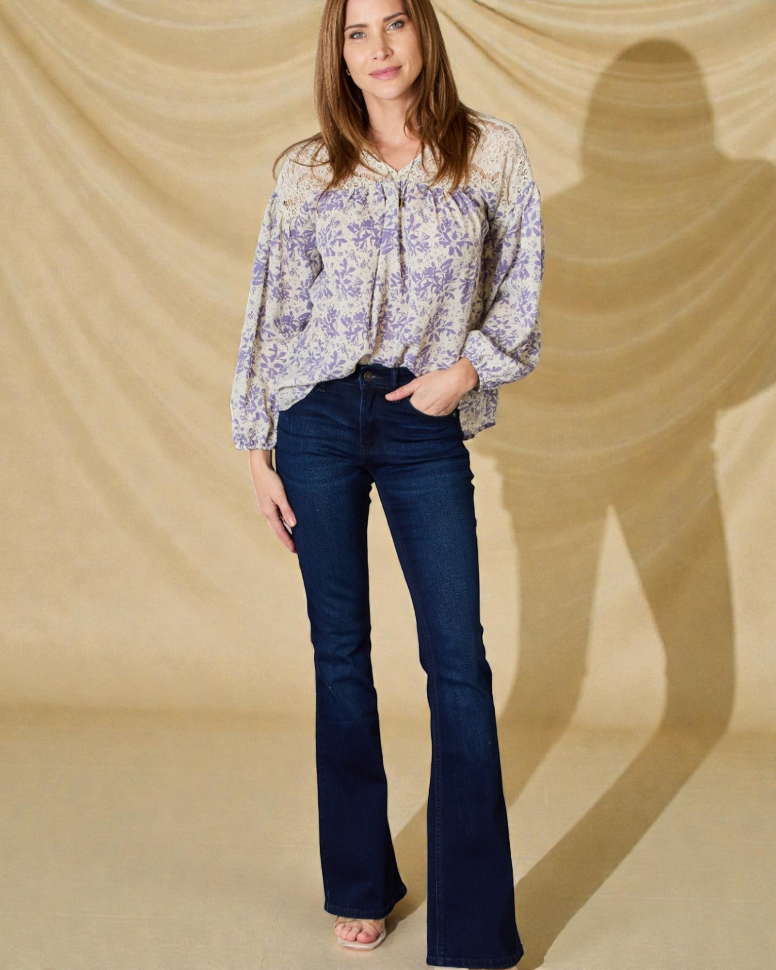 Woman wearing a floral blouse and dark blue jeans against a beige background