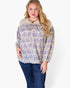A woman modeling a long-sleeve blouse with a purple floral pattern on a cream background, featuring a lace-trimmed round neckline and gathered sleeves, paired with dark blue jeans against a plain white studio background.