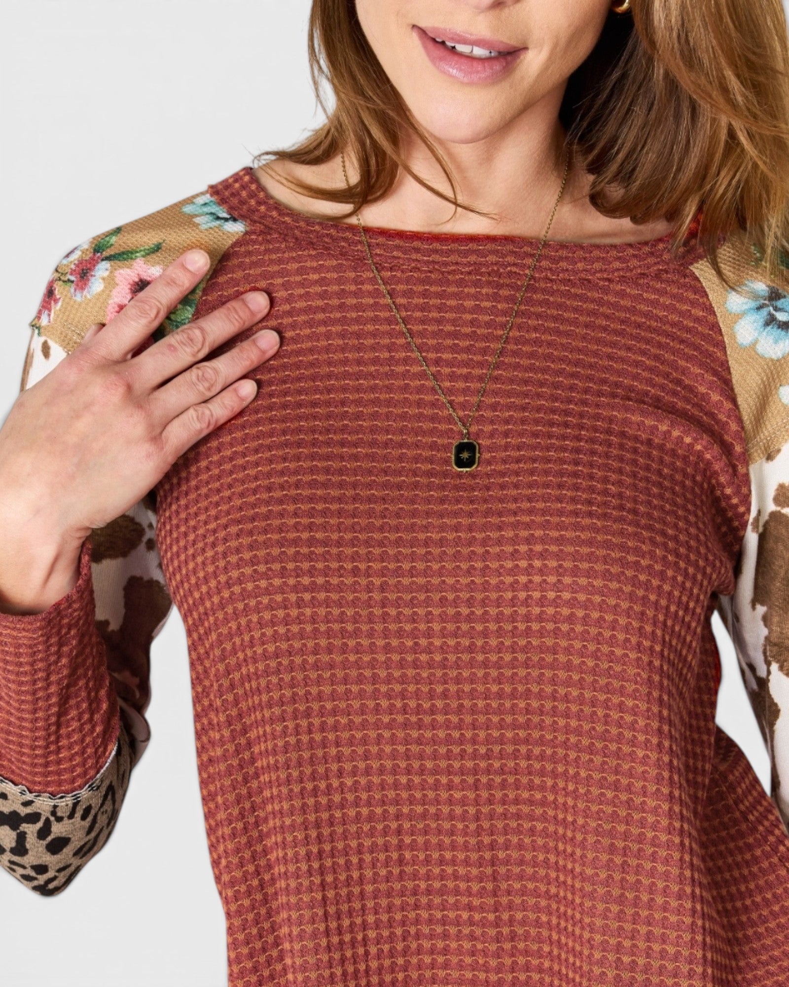 Woman wearing a rust-colored textured top with floral and leopard print sleeves on a white background