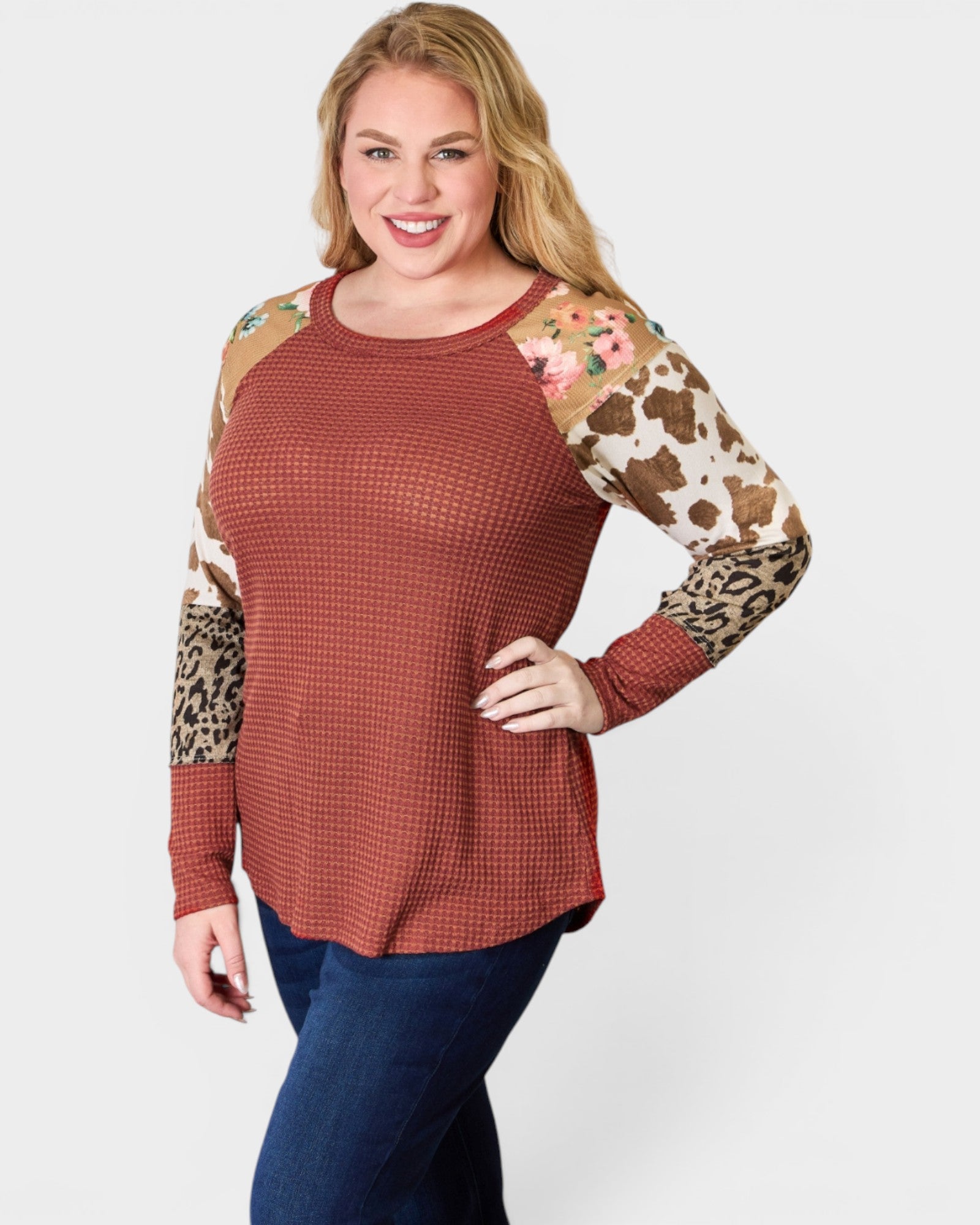 Woman wearing a rust-colored long-sleeve top with animal print sleeves on a white background