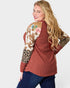 Woman wearing a patterned top with floral, cow print, and leopard print sleeves on a white background