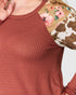 Close-up of a red textured shirt with floral and cow print sleeves.