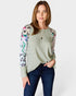 Woman wearing a green sweater with floral and animal print sleeves on a white background
