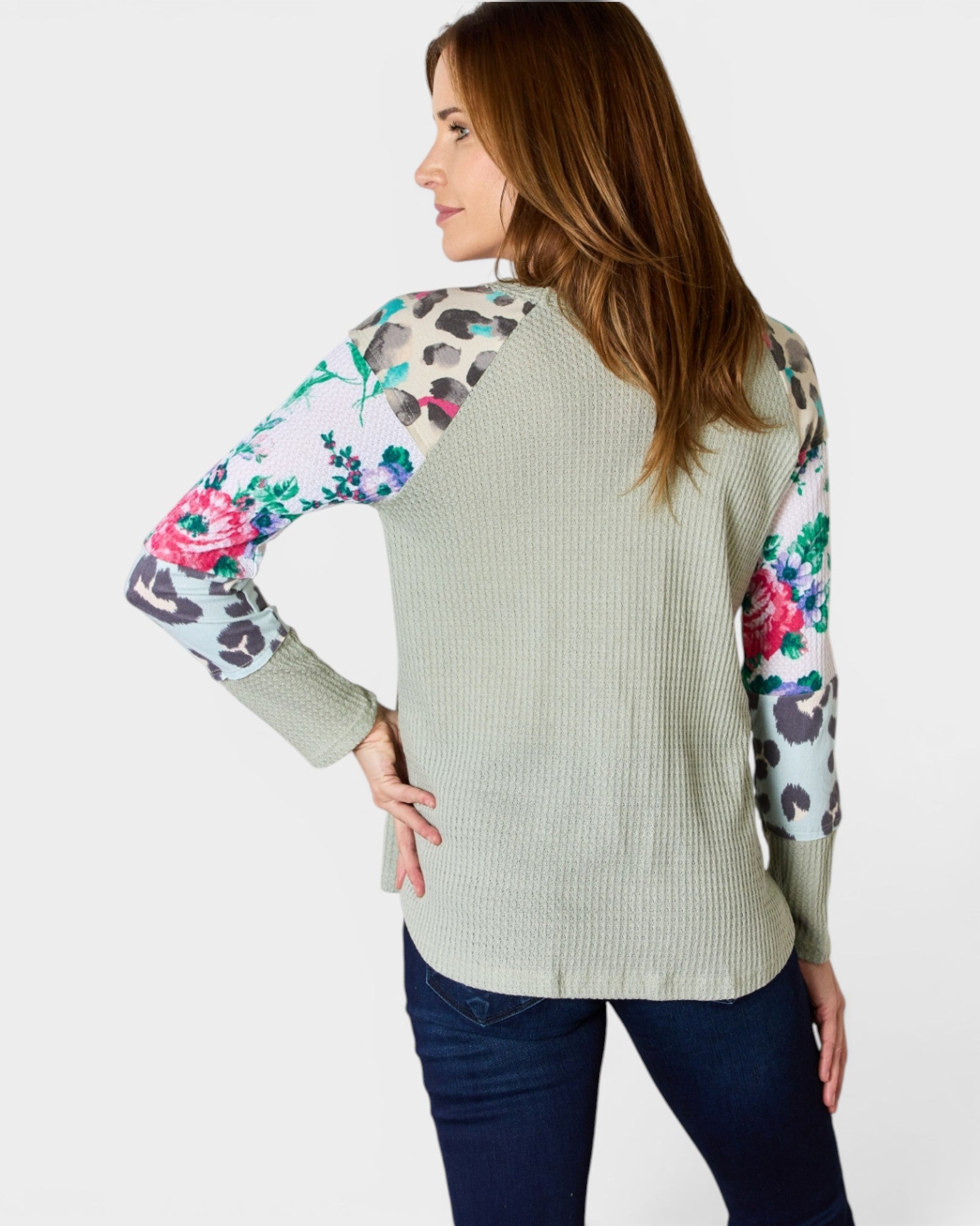 Woman wearing a light green sweater with floral and animal print sleeves on a white background