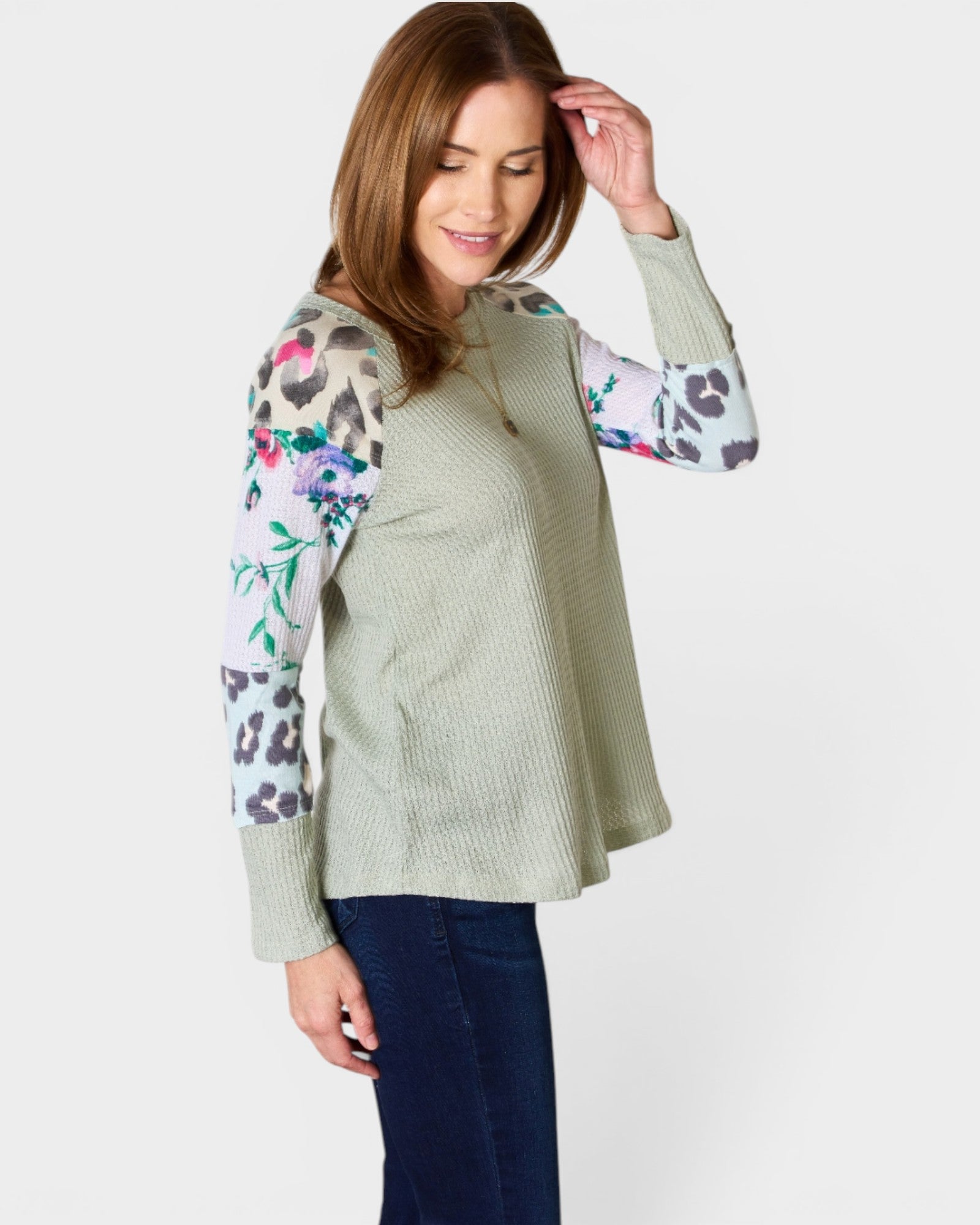 Woman wearing a light green vest over a colorful long-sleeve shirt on a white background