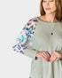 Woman wearing a light green sweater with floral sleeves on a white background