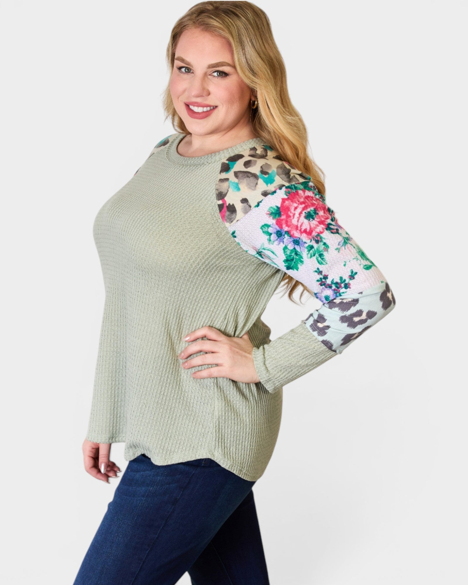 Woman wearing a green sweater with floral and leopard print sleeves on a white background