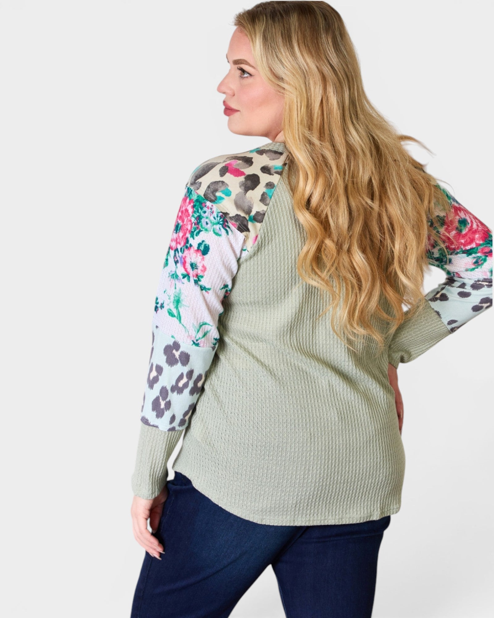 Woman wearing a light green sweater with floral and animal print sleeves on a white background