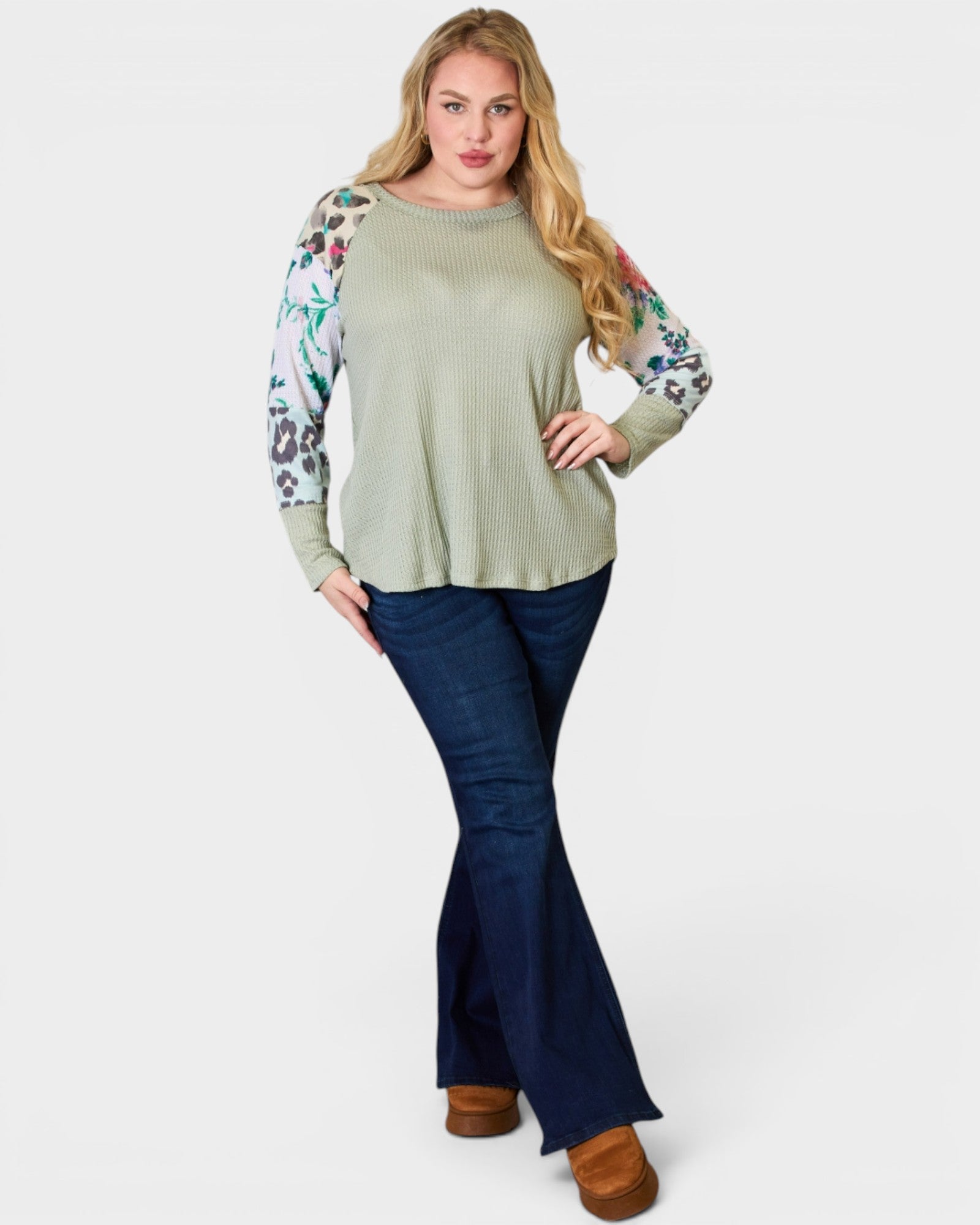 Woman wearing a green sweater with floral sleeves and blue jeans on a white background