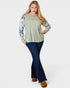 Woman wearing a green sweater with floral sleeves and blue jeans on a white background