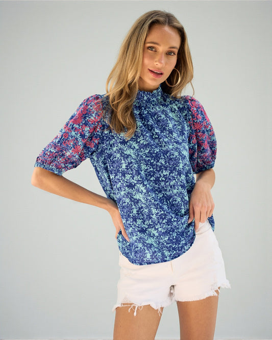 Woman wearing a blue floral blouse with white shorts on a gray background