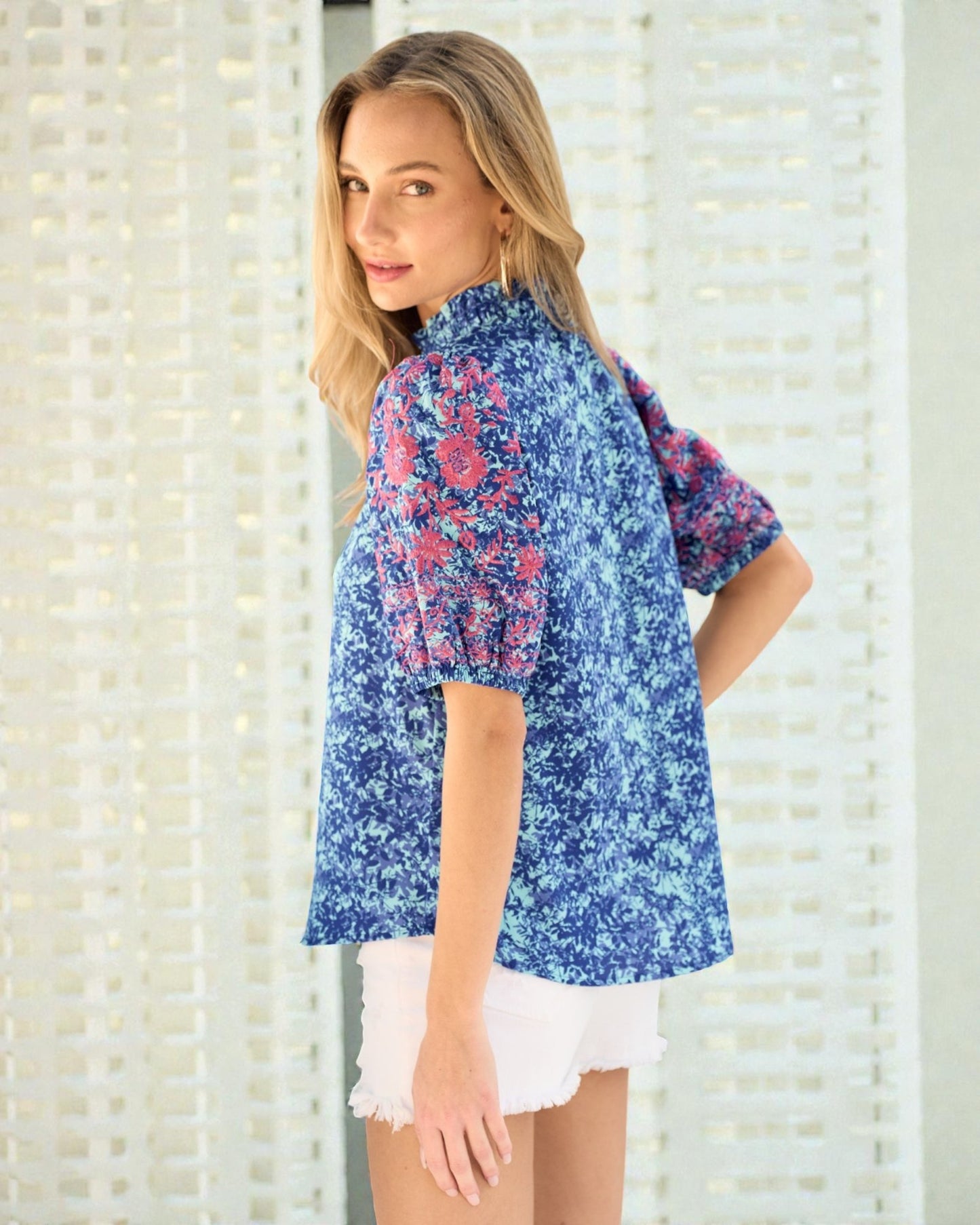 Woman wearing a blue floral blouse with white shorts against a light background