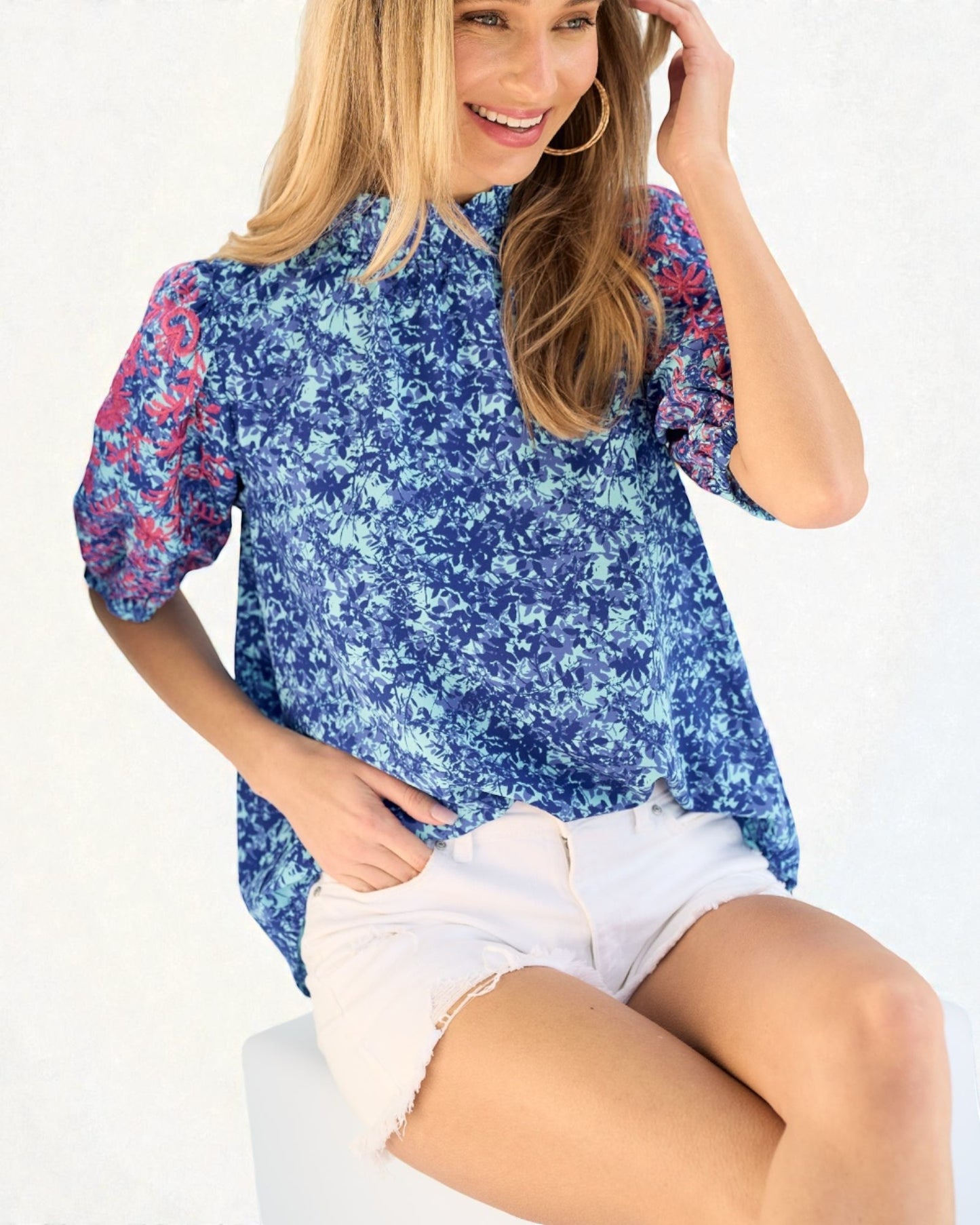 Woman wearing a blue floral blouse and white shorts on a white background