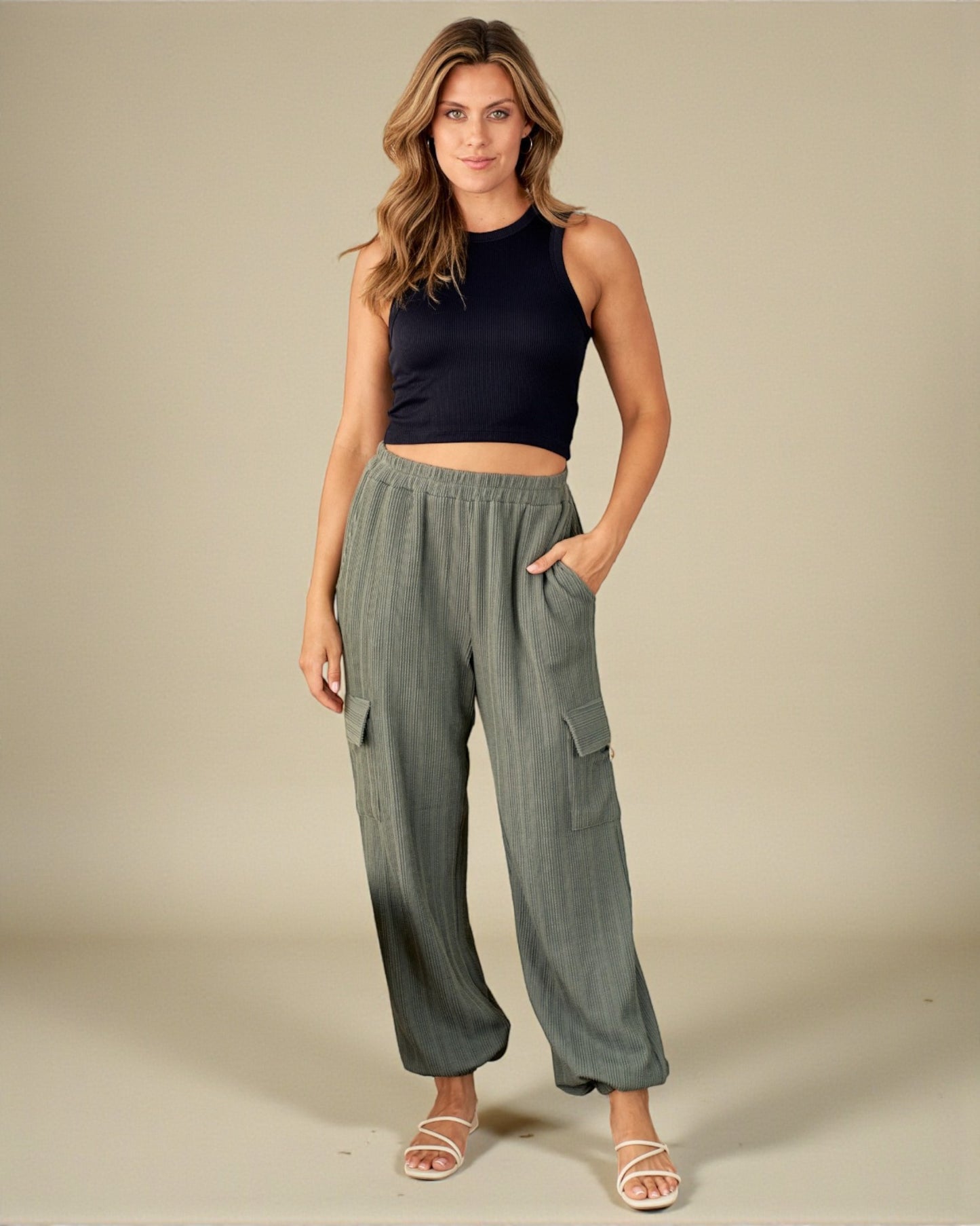 Woman wearing a black sleeveless top and green wide-leg pants on a beige background