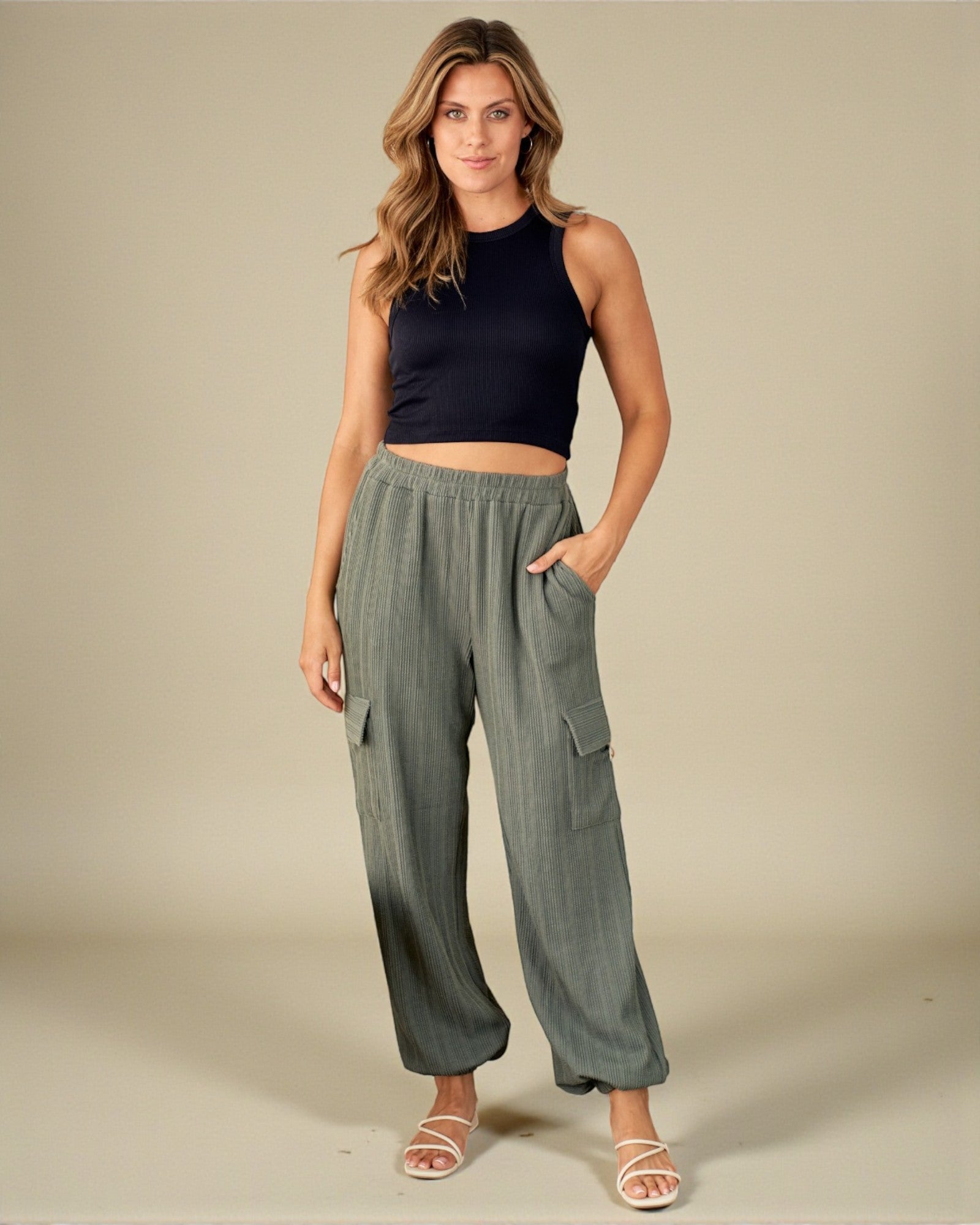 Woman wearing a black sleeveless top and green wide-leg pants on a beige background