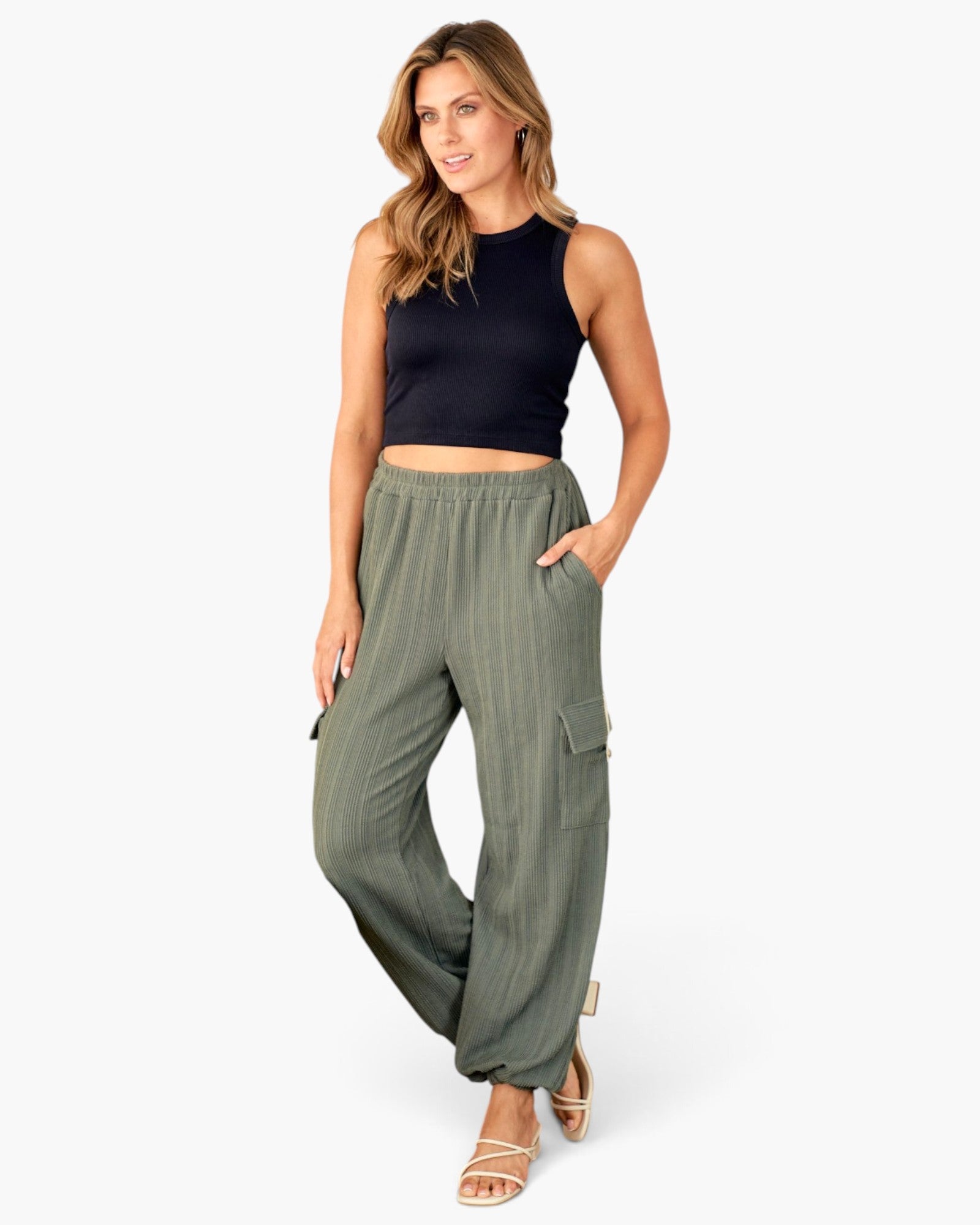 A woman modeling a pair of olive green wide-leg cargo pants with a black sleeveless crop top, standing against a plain white studio background.