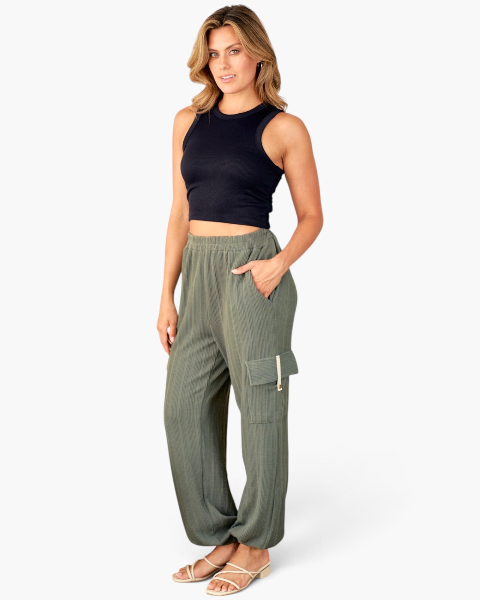 A woman modeling a pair of olive green wide-leg cargo pants with a black sleeveless crop top and beige flat sandals, standing against a plain white studio background.