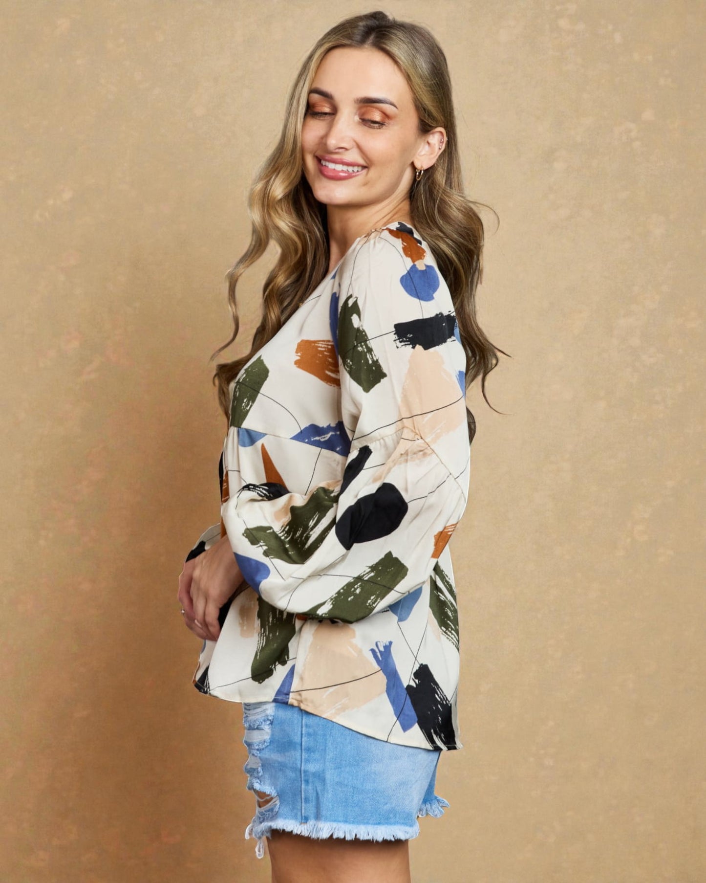 Woman wearing a colorful patterned top and denim shorts against a beige background