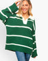 A woman wearing an oversized green and white striped knit sweater with a polo-style collar, paired with blue jeans, against a plain light gray background.