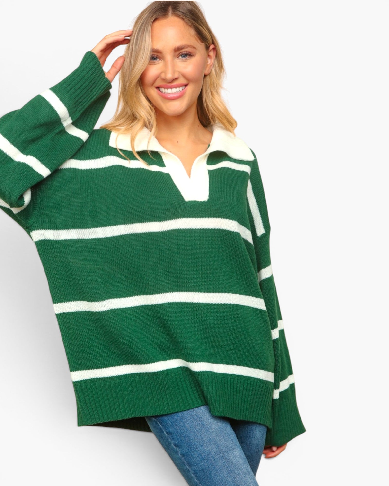 A woman wearing an oversized green and white striped knit sweater with a white collar, paired with blue jeans, against a light gray studio background.