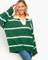 A woman wearing an oversized green and white striped knit sweater with a white collar, paired with blue jeans, against a light gray studio background.