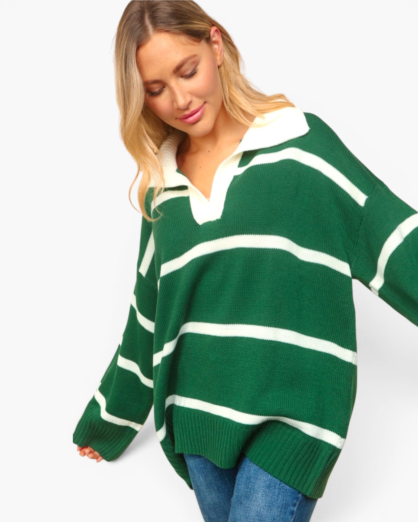 A woman wearing an oversized green and white striped knit sweater with a polo-style collar, paired with blue jeans, against a plain light background.
