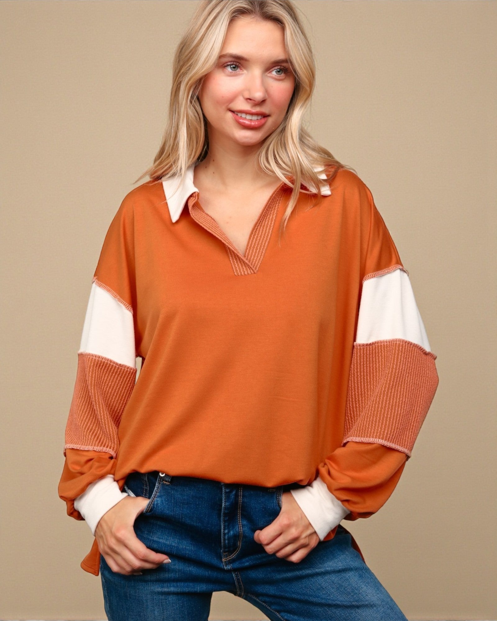 Woman wearing an orange and white long-sleeve top with blue jeans on a beige background