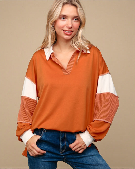 Woman wearing an orange and white long-sleeve top with blue jeans on a beige background