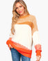 A woman modeling a color-block knit sweater with a cream body, mustard yellow upper chest and yoke, and bright orange ribbed trim at the hem and cuffs, paired with blue jeans against a light gray studio background.